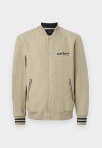Beige varsity jacket with a textured fabric, snap buttons, embroidered logo on the chest, and contrasting striped cuffs.