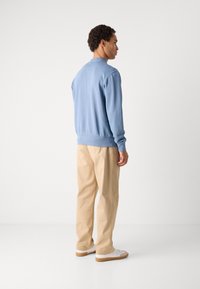 Ανοιχτό μπλε φούτερ με ραμμένα μανίκια και τελείωμα, σε συνδυασμό με μπεζ παντελόνι. Λευκά αθλητικά παπούτσια με μπεζ σόλες. Απλός και καθημερινός σχεδιασμός.