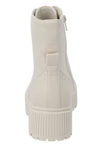 Bottine blanche en similicuir avec fermeture éclair latérale, semelle striée texturée et design minimaliste. Vue de dos montrant un détail de languette au-dessus du talon.