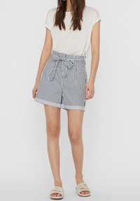 Valkoinen lyhythihainen t-paita yhdistetty tummansinivalkoraidallisiin korkeavyötäröisiin shortseihin, joissa on etuosassa rusetti ja sivutaskut.