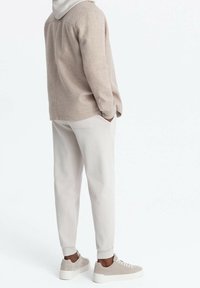 Beiges Fleece-Hemd mit Knöpfen und Kapuze, kombiniert mit hellbeigen, zulaufenden Hosen und grauen Wildleder-Sneakers, Rückansicht.