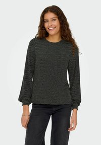 Zwarte trui met geometrisch zilver patroon, lange pofmouwen, ronde halslijn en getailleerde taille, gecombineerd met zwarte jeans.