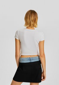 Weißes kurzärmliges Crop-Top, kombiniert mit einem schwarzen Rock mit einem Denim-Bund, der ein einfaches, lässiges Design präsentiert.