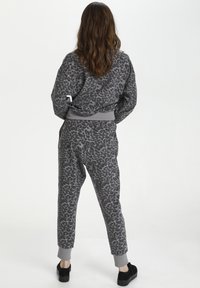 Grå leopardprint træningsdragt med afslappet pasform. Sweatshirt har ribbede manchetter, mens bukserne har elastiske ankler og snor i taljen.
