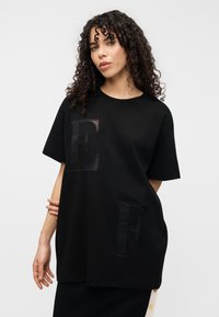 Μαύρο υπερμεγέθες T-shirt από βαμβάκι, με μεγάλα κεντημένα γράμματα "E" και "F" σε αντίθετο χρώμα στο μπροστινό μέρος. Απλός σχεδιασμός με στρογγυλή λαιμόκοψη.