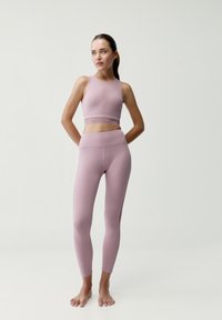 Jasnoróżowy stanik sportowy o dopasowanym kroju z teksturowanym pasem, zestawiony z dopasowanymi legginsami o wysokim stanie, gładkim materiale i bezszwowych akcentach.