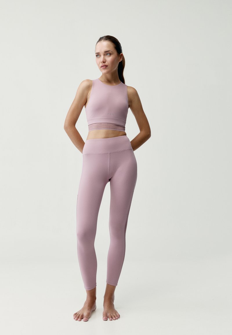 Jasnoróżowy stanik sportowy o dopasowanym kroju z teksturowanym pasem, zestawiony z dopasowanymi legginsami o wysokim stanie, gładkim materiale i bezszwowych akcentach.