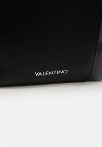 Borsa a tracolla nera in pelle con una superficie testurizzata. Presenta un logo "VALENTINO" in argento ben visibile. Design semplice con dettagli lisci.