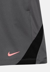 Pantalones cortos deportivos grises con un tejido texturizado, un acento negro y un logotipo de Nike rosa en la parte inferior izquierda.
