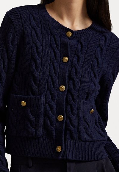 Sini merino jakku, jossa on kultaiset napit, kahdella etutaskulla ja koko vaatteen kattavalla tekstuurilla. Ribbireunat kauluksessa ja helmassa.