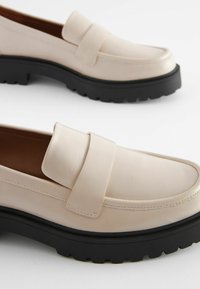 Beige nahkakeng�ät, joissa on leveä hihna ylhäällä, matala musta kumipohja ja hienovarainen tikkausreuna.