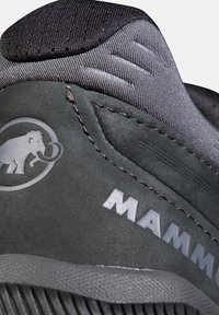 Primo piano del tallone di una scarpa grigia Mammut che mostra tessuto testurizzato, materiale in camoscio, cuciture e logo del mammut.