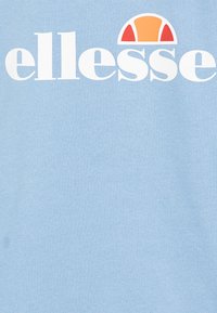 Blå bomullströja med stort vitt "ellesse"-logotyp och en orange halvcirkelgrafik ovanför. Mjuk textur med minimalt mönster.