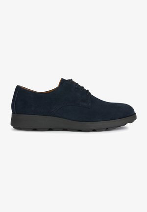 Zapatos de ante azul marino con punta redondeada, diseño minimalista de cordones y una suela de goma negra acolchada, que presenta sutiles acentos de costura.