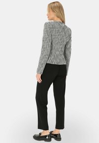 Szara teksturowana kurtka z dopasowaną talią, zestawiona z czarnymi spodniami o prostych nogawkach i błyszczącymi czarnymi butami. Prosty, strukturalny fason z długimi rękawami.