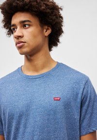 Sinine lühikeste varrukatega T-särk, mis on valmistatud tekstureeritud kangast, vasakul rinnal on väike punane Levi's logo. Ümar kaeluse disain.