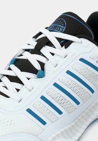 Sapatilha de corrida branca e preta com detalhes azuis. Apresenta uma textura suave, seis atacadores brancos e uma sola com padrão. Detalhes refletivos na lateral.