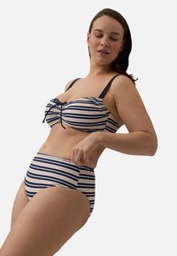 Conjunto de bikini a rayas que incluye un sujetador acolchado con un nudo en la parte frontal y unos pantalones de cintura alta, en colores azul marino y crema, con una textura de tela suave.