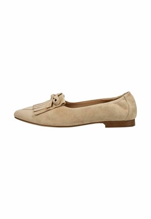 Zapato plano de ante beige con punta puntiaguda, flecos decorativos y detalle de lazo en la parte superior, y un tacón bajo marrón.