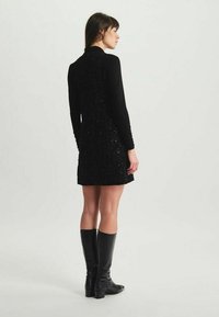 Robe en sequins noir avec des manches longues, un corsage ajusté et une jupe évasée. Associée à des bottes noires jusqu'aux genoux. Texture lisse, finition très brillante.