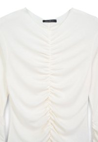 Top bianco a maniche lunghe con scollatura a V e texture arricciata sul davanti, realizzato in tessuto morbido e leggero. Etichetta che riporta "CALLIOPE S."