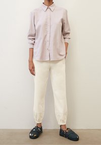 Camicia button-up rosa chiaro con colletto e maniche lunghe, abbinata a pantaloni cream a gamba affusolata e scarpe slip-on navy con motivo.