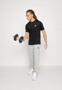 T-shirt sportivo nero con logo, pantaloni tuta grigi, tiene un manubrio. Le scarpe sono sneakers bianche. Design semplice e sportivo.