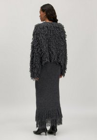 Donkergrijze gebreide trui met gestructureerde franjes, gecombineerd met een bijpassende lange, franje rok. Zwarte enkellaarsjes maken de outfit compleet.