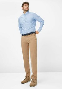 Hellblaues Hemd mit Knöpfen, khakifarbene Hose, marineblauer Gürtel und braune Schnürschuhe. Das Outfit ist lässig und tailliert, mit einer sauberen Passform.