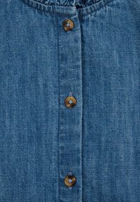 Denim srajca z gumbnim zapiranjem spredaj, ki ima rjave gumbe in teksturirano modro površino. Preprost dizajn, okrogla izreza in brez vzorcev.