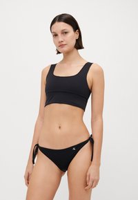 Black bikini set featuring a cropped top with wide straps and a low scoop neckline, paired with tie-side bikini bottoms. Soft, smooth fabric.