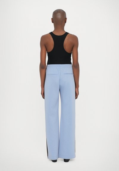 Calças largas de tom azul claro com um tecido texturizado, apresentando uma cintura elástica e dois bolsos traseiros, combinadas com uma blusa preta de alças.