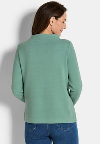 Muntgroene langemouwtop met een gestructureerd ribbelontwerp, ronde halslijn en een losse pasvorm, gecombineerd met donkerblauwe spijkerbroek.