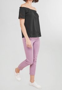 Haut noir décolleté aux épaules avec bordure en dentelle ; associé à un pantalon moulant violet clair et des baskets blanches. Tissu lisse, coupe décontractée.