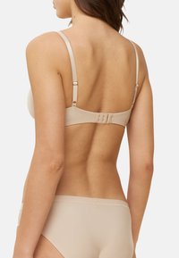 Sutia acolchado beige con tirantes ajustables, cierre de gancho y ojo en la parte posterior, textura suave y sutiles acentos de hardware.