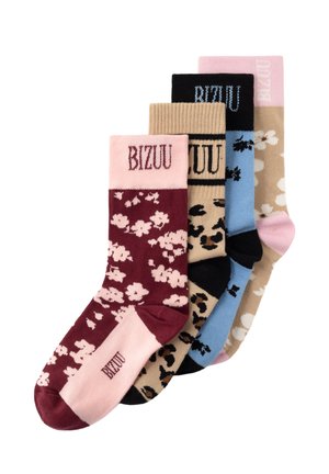 Nogi noszące bordo i różowe kwieciste skarpetki z tekstem "BIZUU", w zestawieniu z beżowymi, sznurowanymi, zamszowymi butami casual.