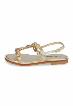 Sandale plate dorée avec bride en T ornée de bijoux, boucle de cheville ajustable et semelle marron clair.