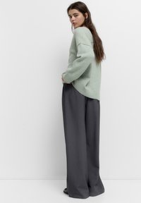 Pulover verde deschis cu umeri căzuți și manșete cu model, asortat cu pantaloni largi gri închis, cu talie înaltă, dintr-un material neted.