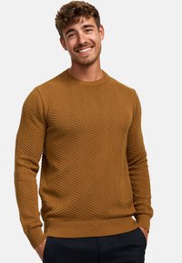 Brown knit sweater with a herringbone pattern, round neckline, and ribbed cuffs and hem. Worn with dark trousers.