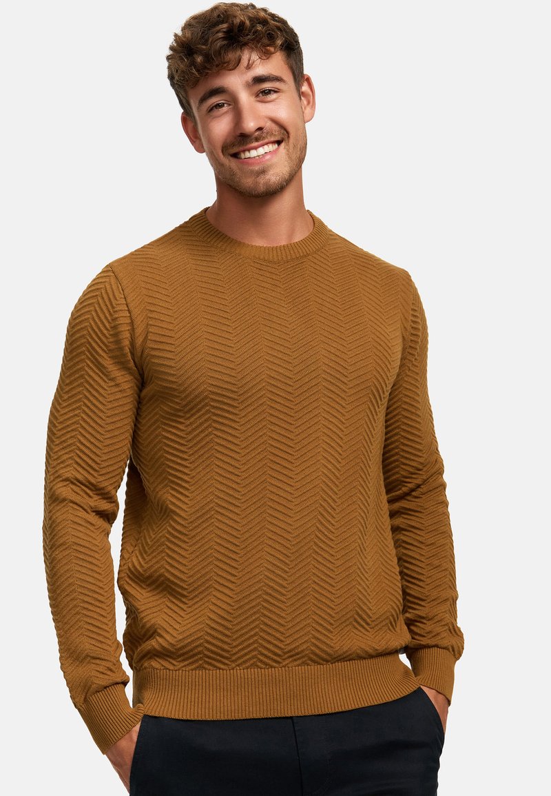 Brown knit sweater with a herringbone pattern, round neckline, and ribbed cuffs and hem. Worn with dark trousers.