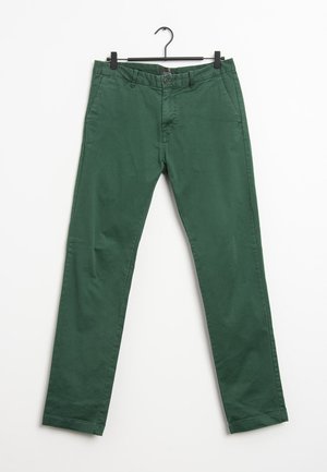 Grüne gerade geschnittene Hose mit seitlichen Taschen und Knopfverschluss, die an einem schwarzen Kleiderbügel vor weißem Hintergrund hängt.