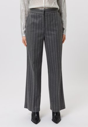 Person wearing high-waist grey pinstripe trousers paired with black pointed-toe ankle boots and a shiny silver long-sleeve top.