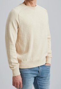 Crèmekleurige trui van zachte gebreide stof, met een ronde hals en geribde manchetten, gecombineerd met lichtblauwe spijkerbroek.