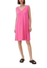 Różowa, bezrękawnikowa sukienka z dekoltem w kształcie litery V, wykonana z miękkiego materiału. Modelka połączyła ją z czarnymi sandałami na płaskiej podeszwie, tworząc prosty wygląd.