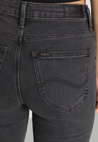 Jeans de mezclilla negra con una cintura alta, bolsillos traseros con costuras curvas y un parche de cuero en la cinturilla.