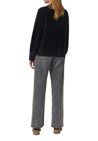 Szary, oversize'owy sweter z dzianiny o pudełkowym kroju, w zestawieniu z szerokimi, szarymi dżinsami. Buty w stonowanym brązowym odcieniu.