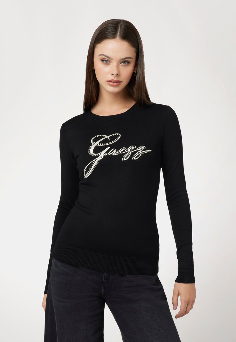 Maglione nero realizzato in tessuto morbido, con maniche lunghe e orlo a coste. La parte anteriore presenta un design del logo in strass argentati.