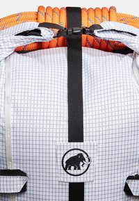 Witte geruite stoffen rugzak met zwarte banden en accenten. Oranje touw is aan de bovenkant bevestigd; logo patch met een olifant aan de voorkant.