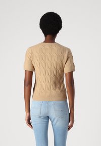 Pull beige à manches courtes avec texture en maille torsadée, col rond et ourlet côtelé. Associé à un jean bleu clair.