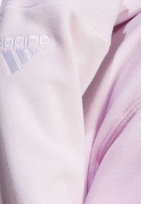 Ljusrosa sweatshirt med mjuk textur, med vit broderad logga och tre ränder design på ärmen.